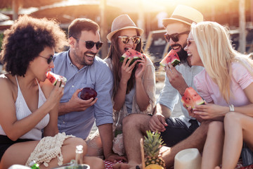 Group of friends eating watermelon on the beach