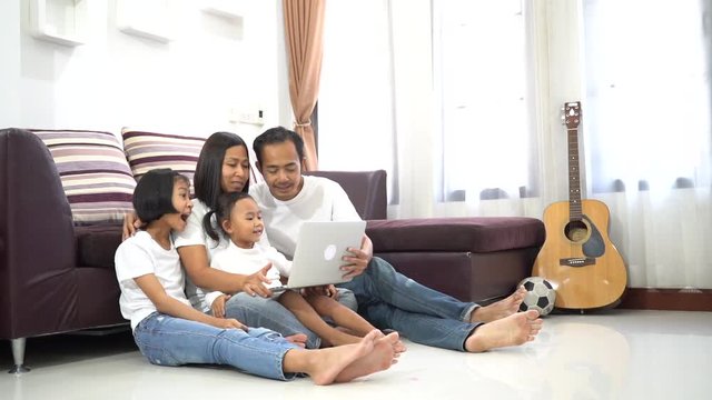 Happy asian family and little daughter are sitting room on a floor at home and using a laptop computer
