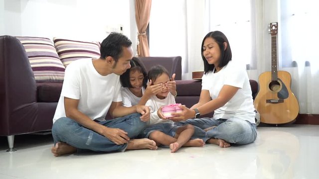 Happy asian family little cute girl with closed eyes give a gift, Sitting room on a floor at home,