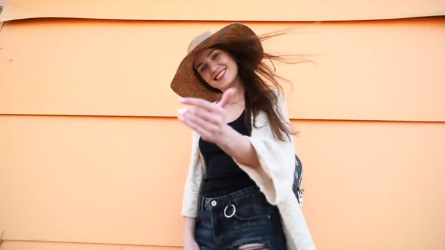Young attractive stylish woman wearing straw hat poiting at camera and calling to follow her on yellow background. Travel concept.