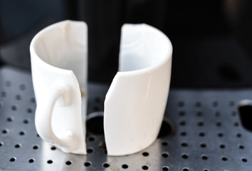 White espresso coffee cup broken in half placed on home espresso machine. Concept of bad morning
