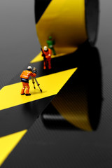Miniature scale model construction workers using hazard tape on a carbon fibre surface