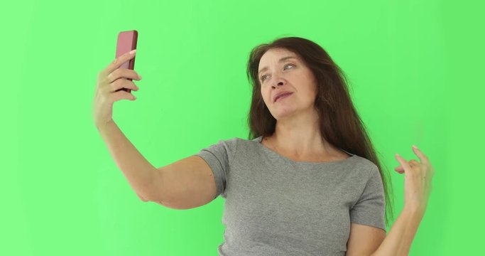 Beautiful senior woman with cellphone taking a selfie isolated on green background