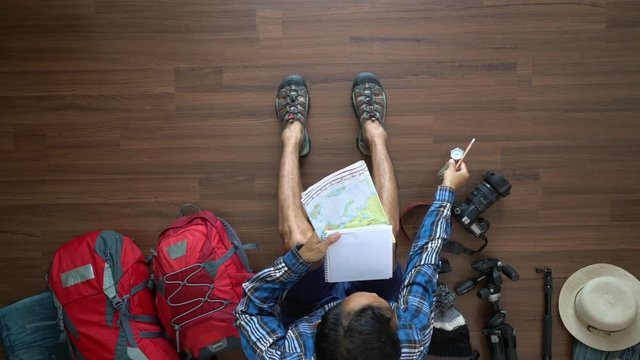 Traveler man and backpack planning vacation travel idea concept trip with map. Top view on wood floor          