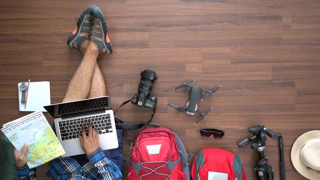 Traveler man and backpack planning vacation travel idea concept trip with working laptop computer. Top view on wood floor