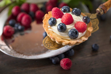  Dessert tarts with raspberries and blueberries on a wooden table.