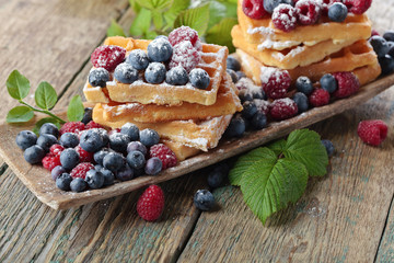  Yummy sweet waffles with raspberries and blueberries on a wooden table .