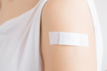 White adhesive bandage on young woman's arm after scratch on skin or injection of vaccine. First...