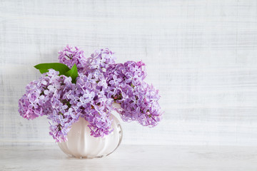 Fresh branches of purple lilac blossoms in vase on wooden table. Vintage greeting card. Mockup for positive ideas. Empty place for inspirational, emotional, sentimental text or quote. Front view.