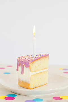 Trozo de pastel de cumpleaños con una vela sobre fondo blanco con confeti
