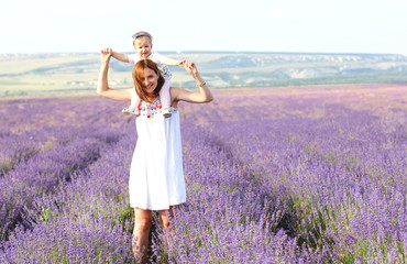 Happy little girl and her mother on lavender background. Cute baby playing in meadow field. Family holiday in summer day.