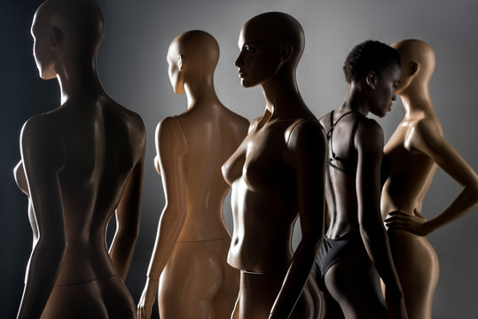 young african american woman in bodysuit standing between dummies on black