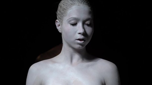 Girl in white body art looks at the camera and looks down behind her is a black man, slow motion