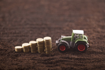 Naklejka premium Tractor miniature with coins on fertile soil land