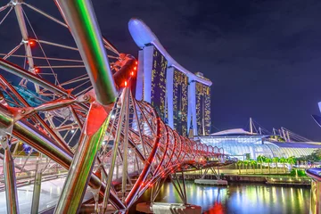 Papier Peint photo Helix Bridge Paysage urbain de Singapour, Asie du Sud-Est. Pont piétonnier illuminé la nuit au premier plan dans la région de Marina Bay. Architecture moderne dans la ville de Sigapore.