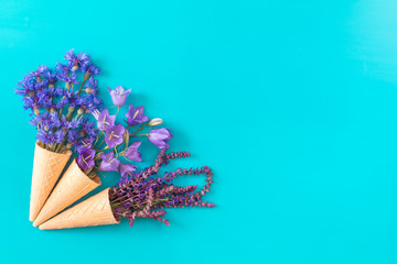 Three waffle cones with flowers blossom bouquets on blue surface.