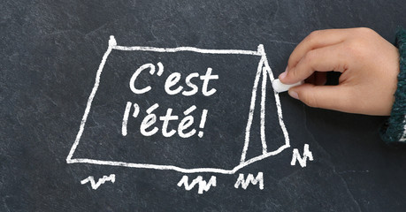 Enfant dessinant une tente avec "c'est l'&eacute;t&eacute;" sur une ardoise