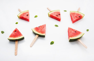 Watermelon slice popsicles and paper mint on white wooden background.