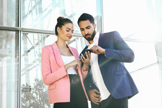 Welcome on board! Two handsome men shaking hands with smile while sitting on the couch at office with their coworkers