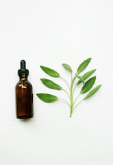 Sage essential oil with sage leaves on white  blackground.