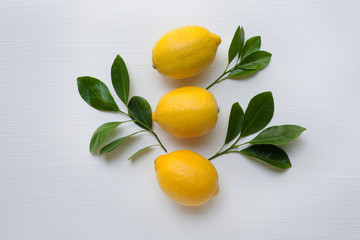 Three yellow lemons with leaf on white.