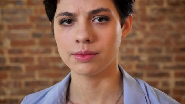 Young serious short hair girl is watching at camera, brick background