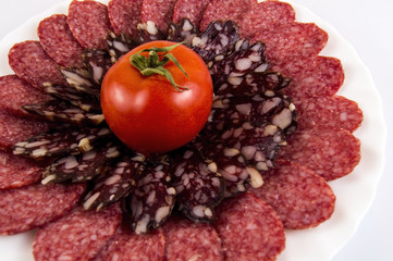 cutting a light and dark sausage with tomato on a white plate