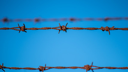 Rusted and barbed wire fencing against a blue sky


