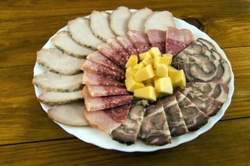 Sausage, baked meat, roll and cheese in a white plate on a wooden background