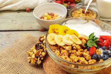 Bowl of homemade granola with yogurt and fresh berries on wooden background