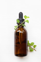 A bottle of oregano essential oil with fresh oregano leaves on white.