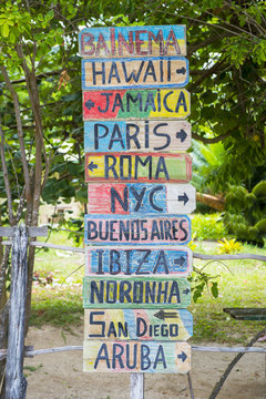 Rustic colorful sign on a beach showing directions to islands and cities around the world