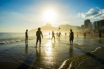  Silhouettes of Brazilians playing keepy uppy altinho beach soccer on the sunset shore on Ipanema Beach © lazyllama