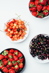 top view of fresh ripe tasty summer berries in bowls on white