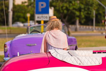 CUBA, HAVANA - MAY 5, 2017: Curly girl on the background of colored cars Cuba, Havana. Back view.