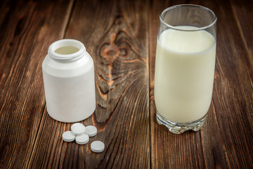 Calcium supplement tablet pills on dark wooden background. White tablets near the inverted jar and glass of milk. Pills or food concept.