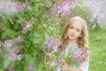 blonde hair girl in a blooming lilac garden