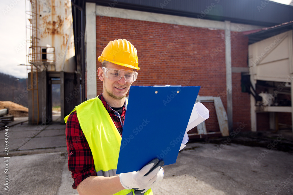 Wall mural Male construction worker looking at clipboard