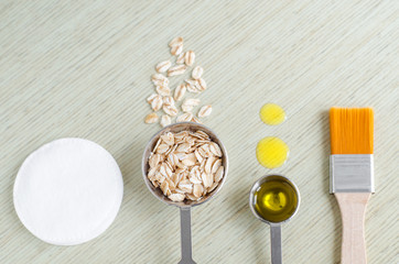 Small scoops with oatmeal and olive oil with cosmetic brush and cotton pad. Ingredients for preparing diy masks, scrubs for natural skin and hair care. Homemade cosmetics concept. Top view, copy space