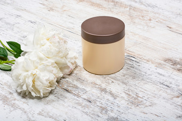 Beige mocap can for cream after skin care face and body and flowers peonies lying on a battered texture light wooden table, view directly, close-up