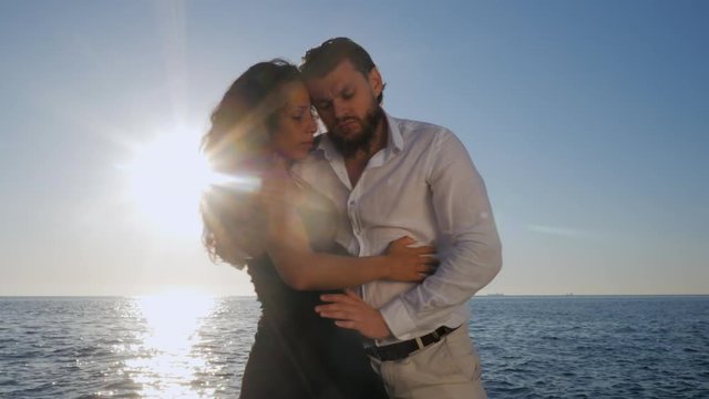 Portrait of young attractive couple dancing latin bachata near sea or ocean. Sunlight background. Summer time, romantic footage. Slow motion.