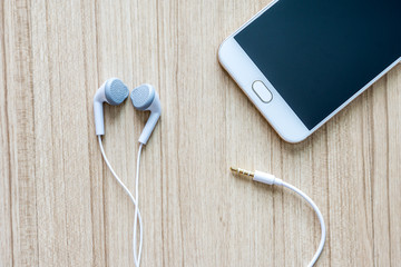 White earphones  with smartphone  on office wooden desk background.