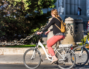 Naklejka na ściany i meble MADRID, SPAIN - SEPTEMBER 26, 2017: A woman is riding a bike on a city street. Copy space for text.