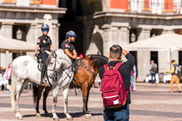 Fototapeta na wymiar MADRID, SPAIN - SEPTEMBER 26, 2017: A man photographs the mounted police in the square of the Royal Palace building.