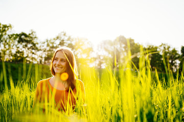 Young woman sitting laughing in the grass in the sunshine