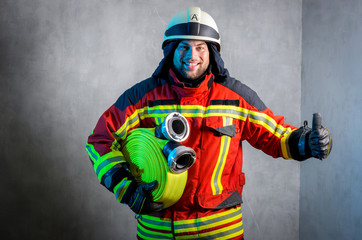 Feuerwehrmann mit gerolltem B-Schlauch unterm Arm lacht in die Kamera und hält den Daumen nach oben
