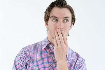 Curious young man covering mouth while listening to gossip. Shocked guy in casual shirt knowing...