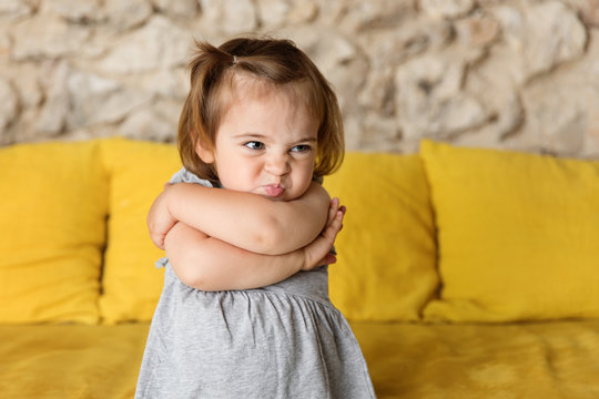 Toddler girl pouting with funny face on yellow couch
