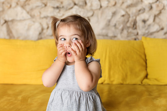 Little girl making funny suprised face on yellow couch