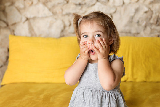 Toddler making funny suprised face on yellow couch